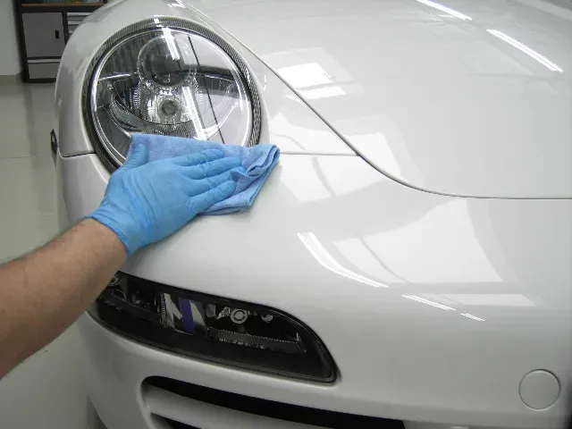 Weißer Porsche wird in der Halle von Hand nachpoliert